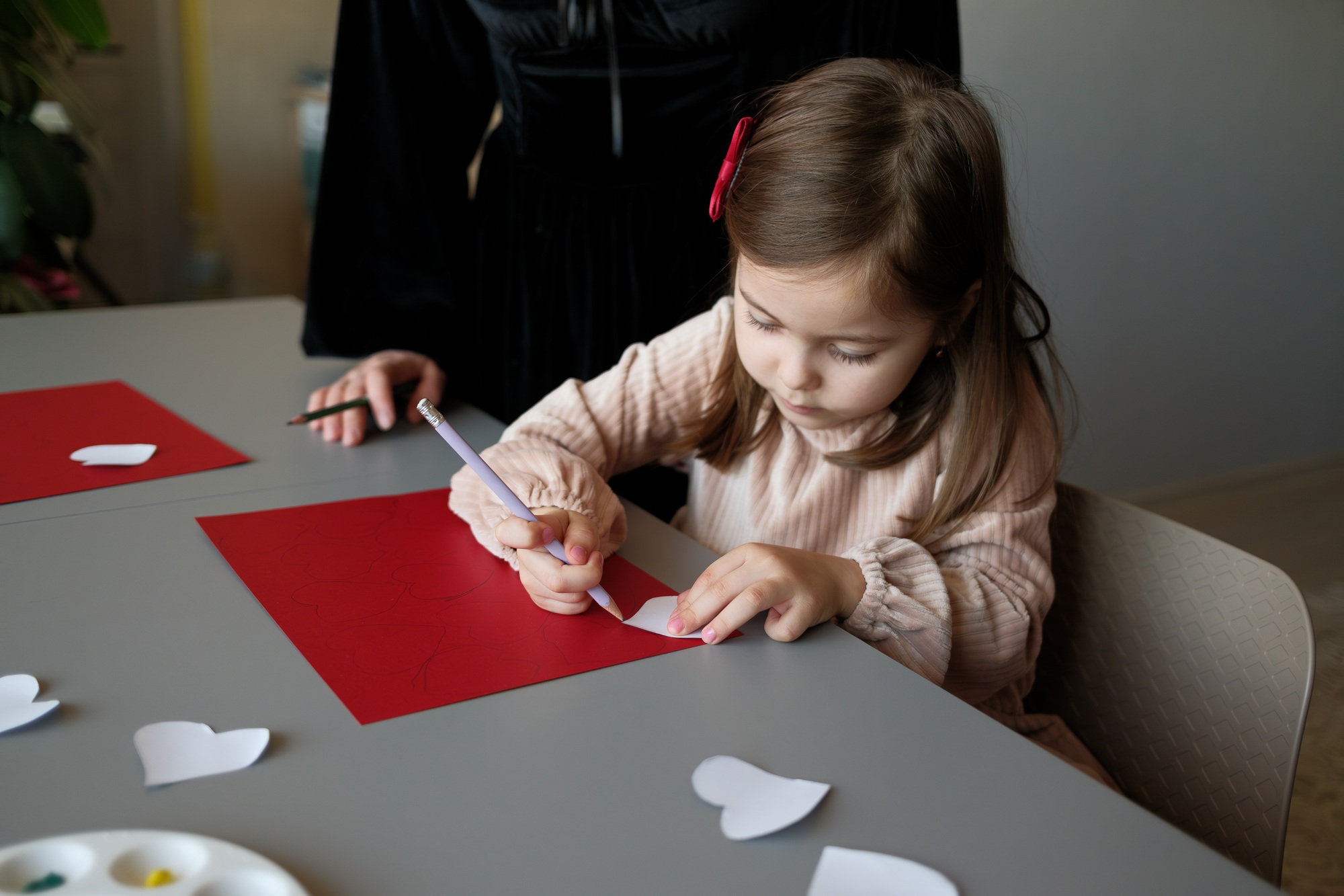 Child engaging in arts and crafts activity with assistance at a table