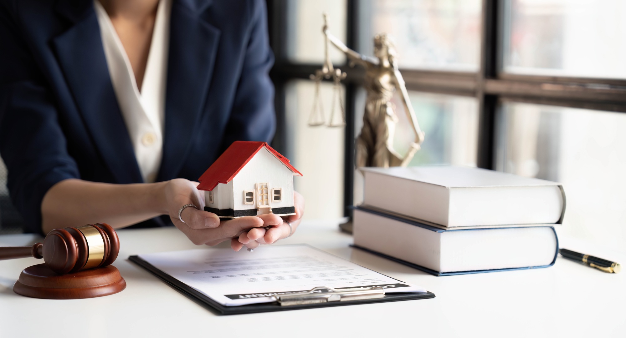 Close-up of and small wooden toy house on table with female lawyer on background and.holding that