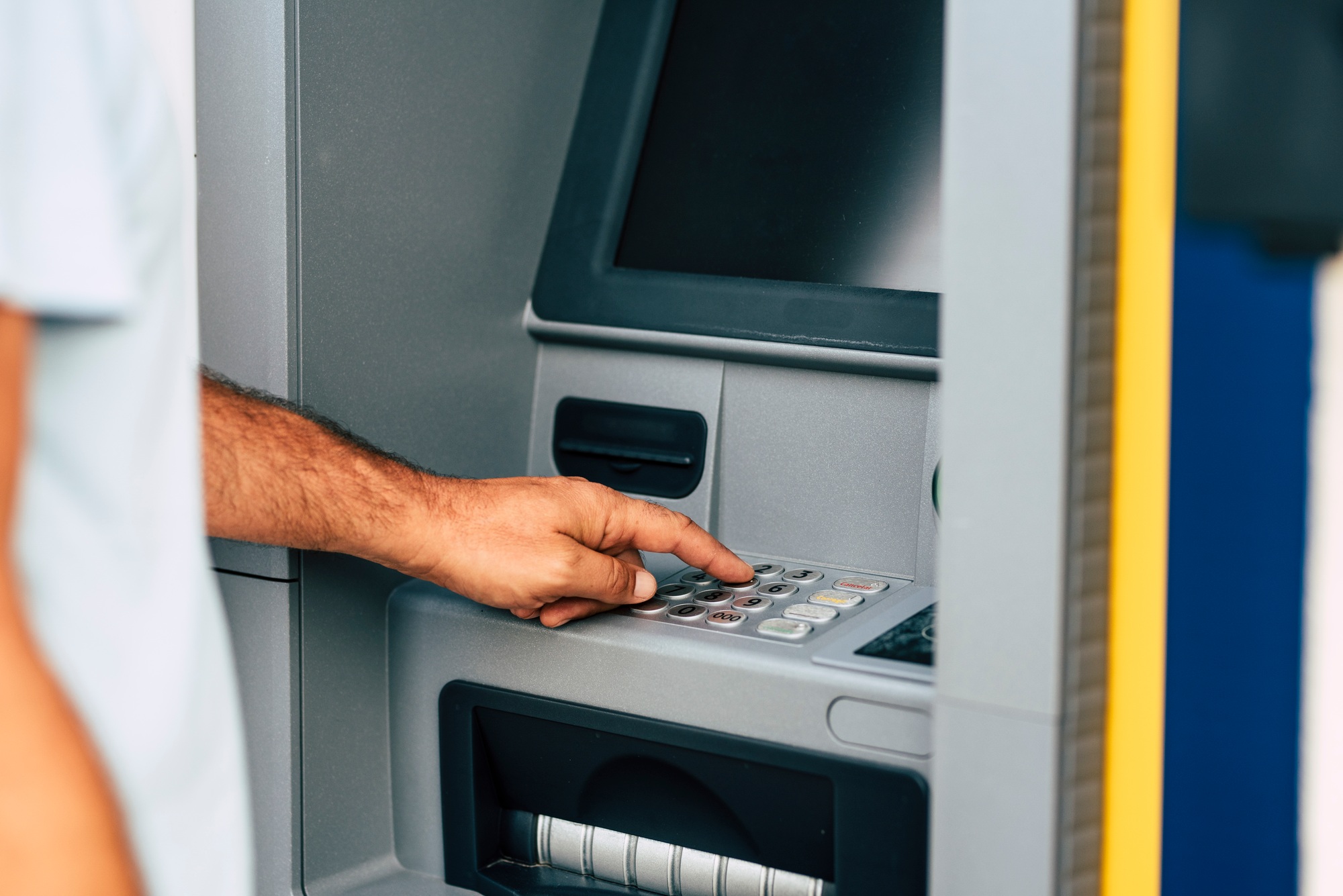 Close up of man hand withdrawing money at automatic atm machine typing secret security code