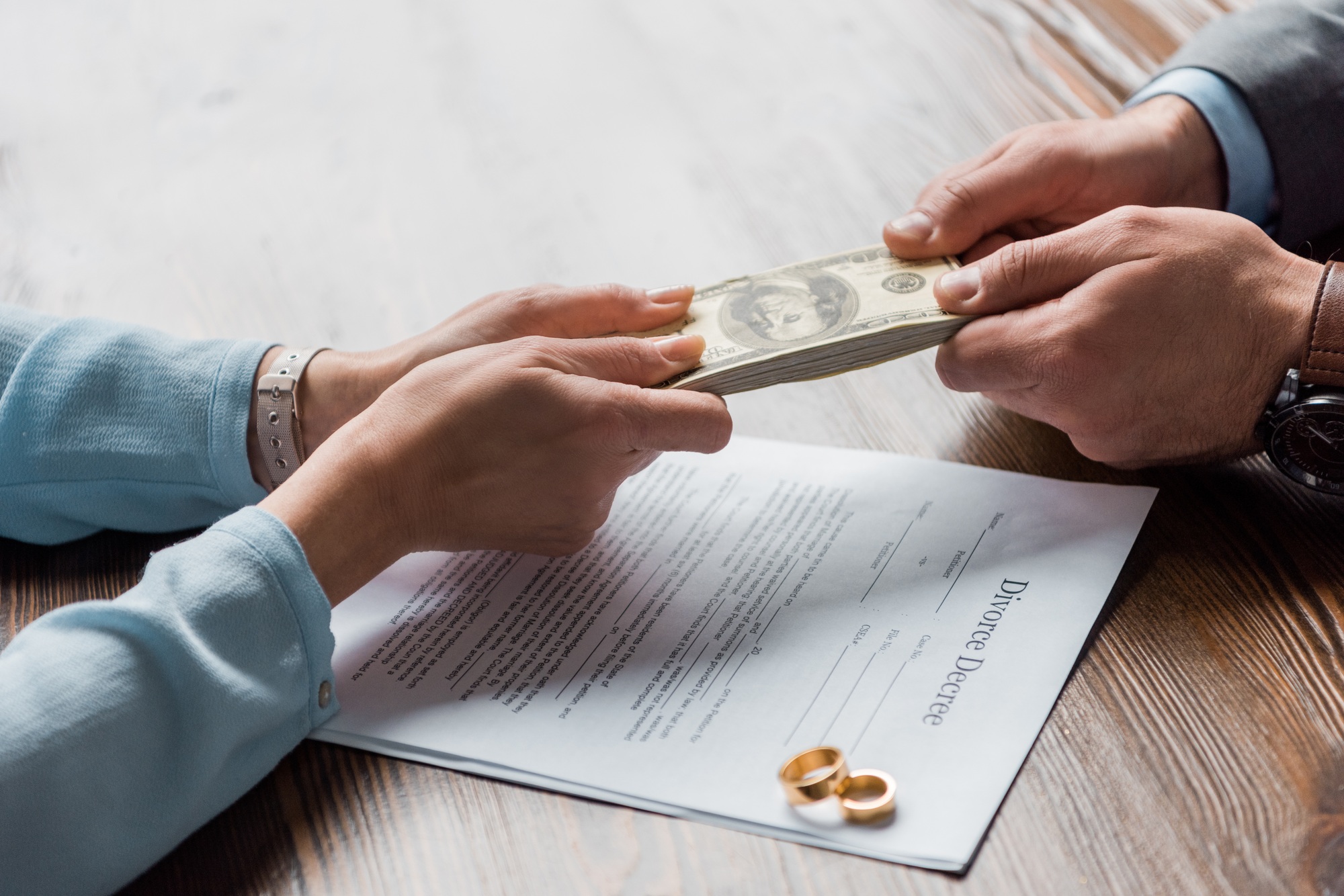 cropped shot of lawyer and client holding dollar banknotes above divorce decree with wedding rings
