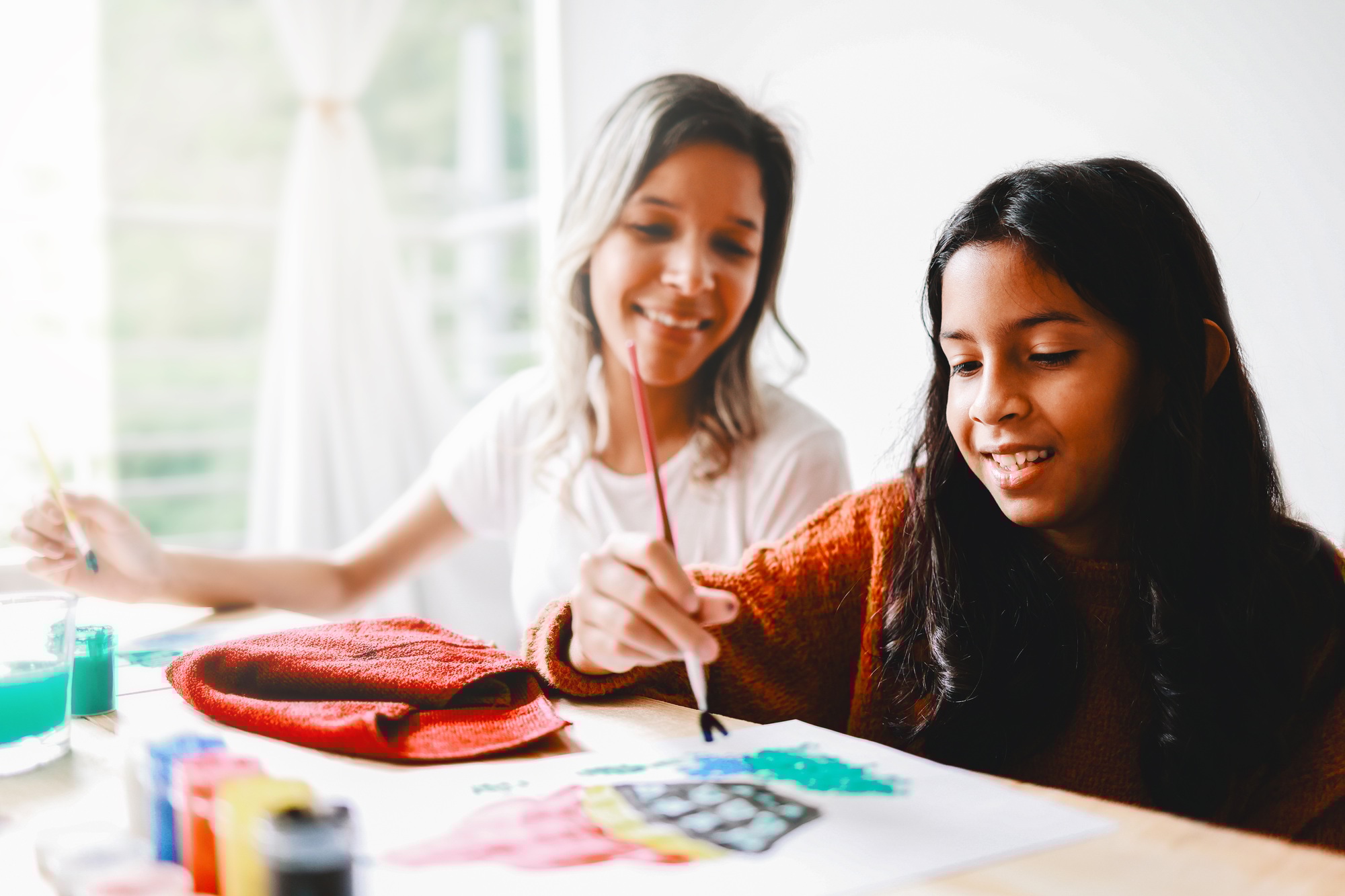 Happy latin mother and daughter having fun painting together at home. Mom, child, love and family