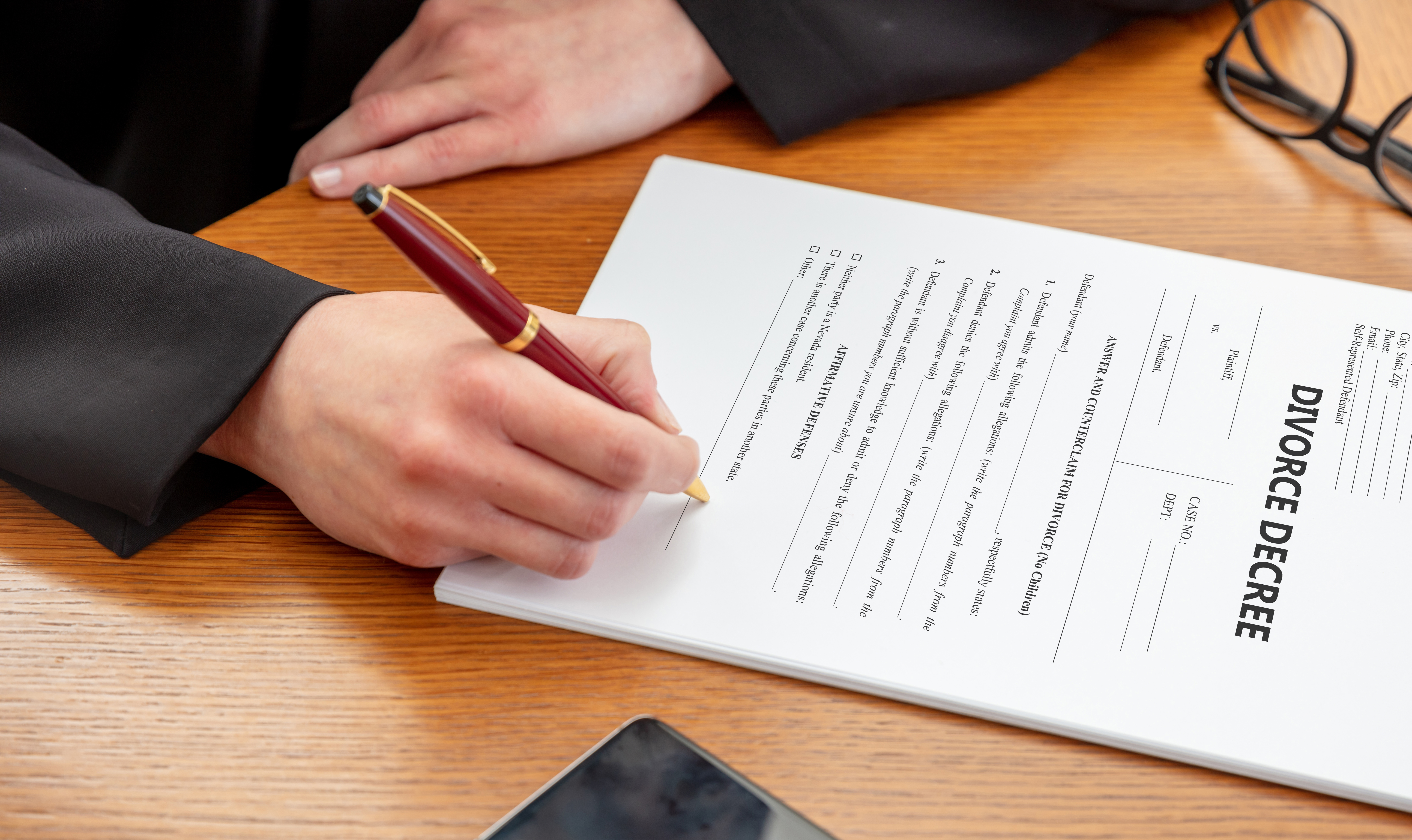 DIVORCE DECREE. Woman signing the paper, Lawyer, notary office. Female hand holding a pen, close up above view, wooden table background.